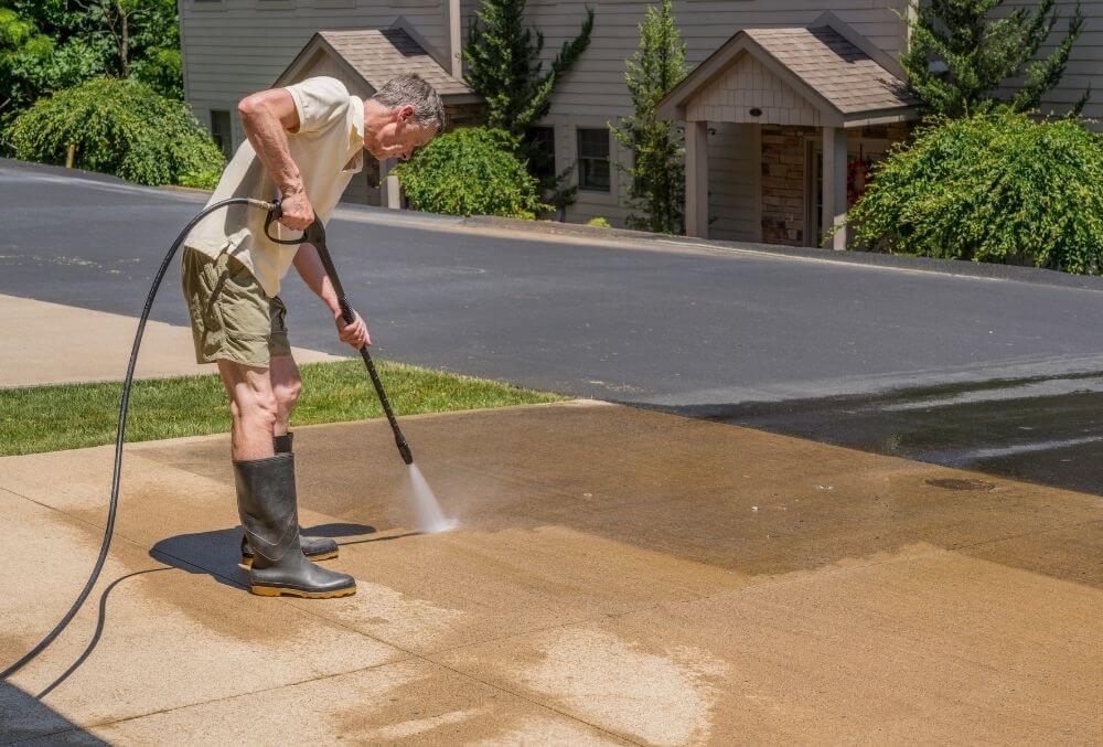 man pressure washing concrete driveway