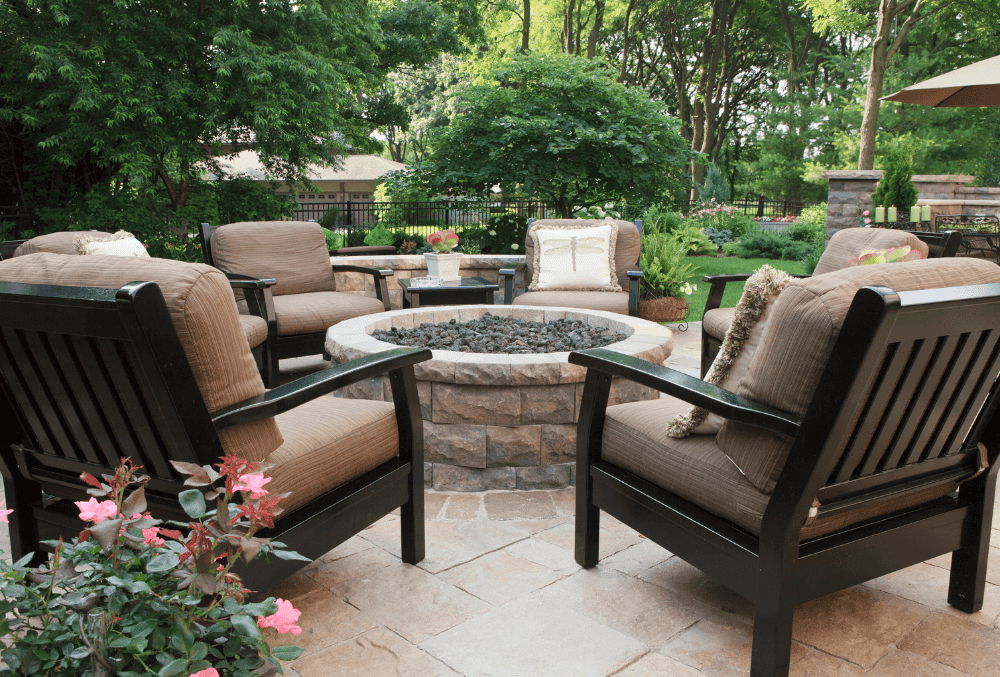 Cozy outdoor seating area with chairs and a fire pit on a beautifully finished concrete patio surrounded by greenery.