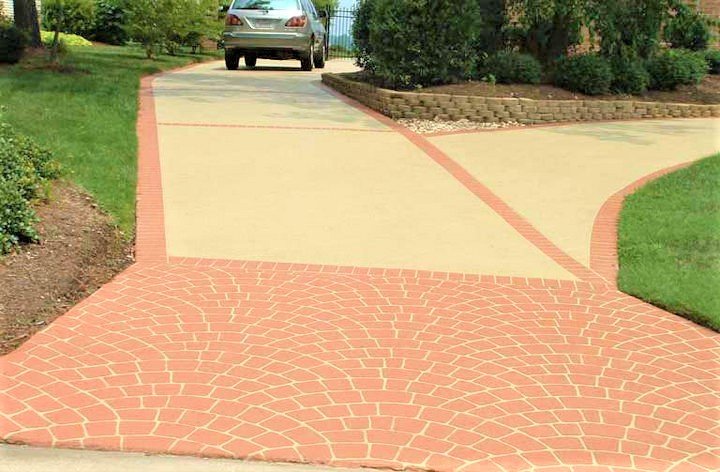 Decorative concrete driveway with brick-patterned border and smooth surface leading to a parked car.