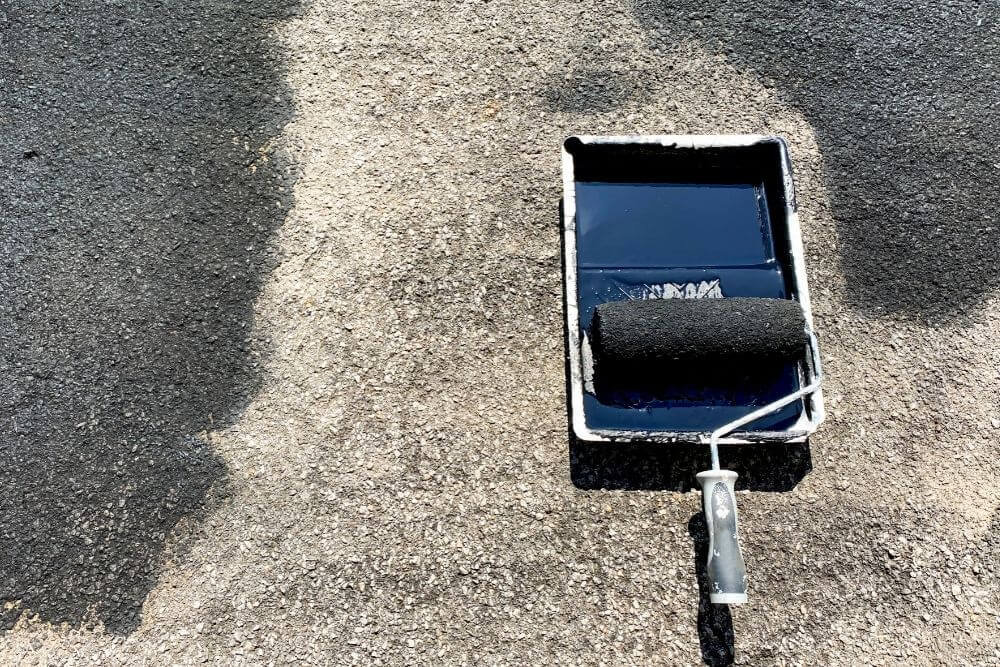 black sealant paint being applied on a concrete driveway