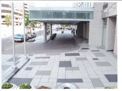 Modern public space with patterned concrete walkway and covered entrance in an urban city area.