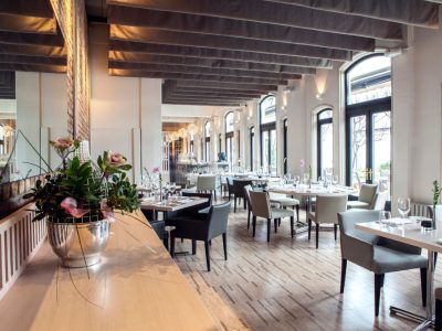 Modern restaurant interior with elegant furniture, large windows, and polished concrete flooring.