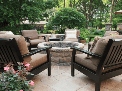 Cozy outdoor seating area with chairs and a fire pit on a beautifully finished concrete patio surrounded by greenery.