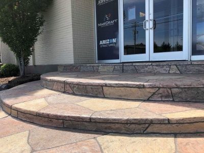 Textured decorative concrete steps leading to a building entrance with natural stone finish