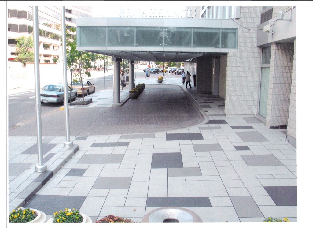 Modern public space with patterned concrete walkway and covered entrance in an urban city area.