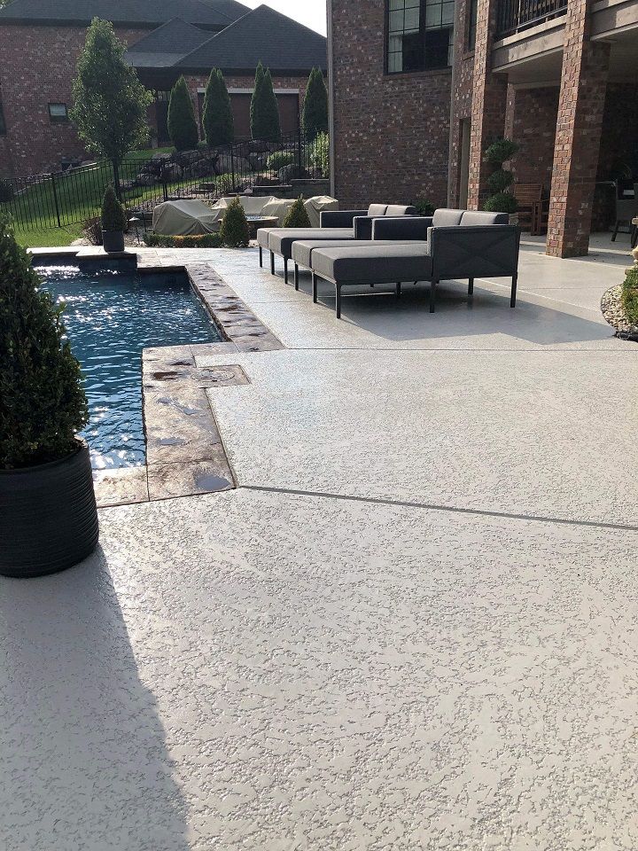 Outdoor pool deck with a spray knockdown textured surface and a cozy sofa seating area beside the pool.