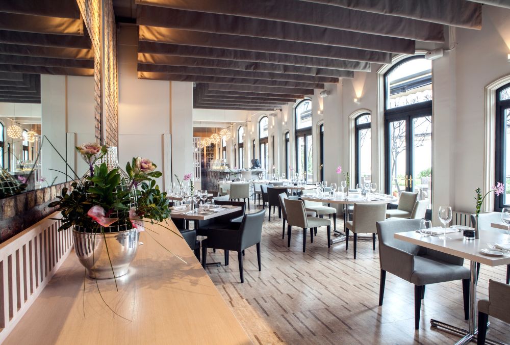 Modern restaurant interior with elegant furniture, large windows, and polished concrete flooring.