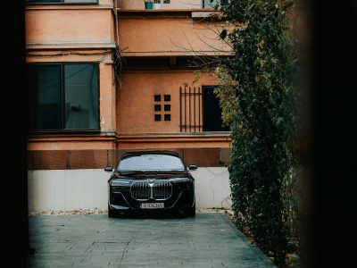 Black luxury car parked on a clean concrete apartment driveway surrounded by trees and residential buildings.